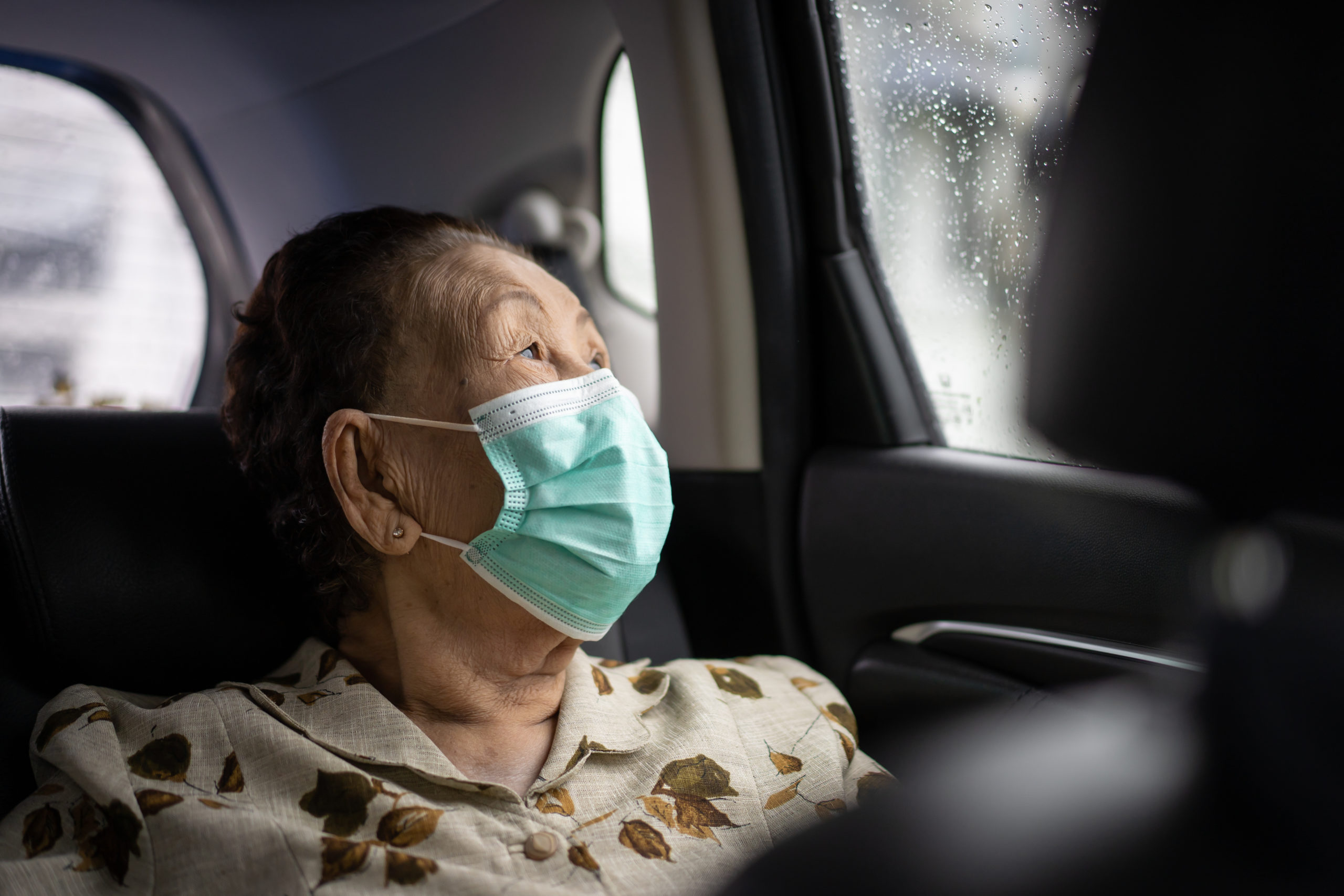 Older woman in van looking out of window and wearing a mask